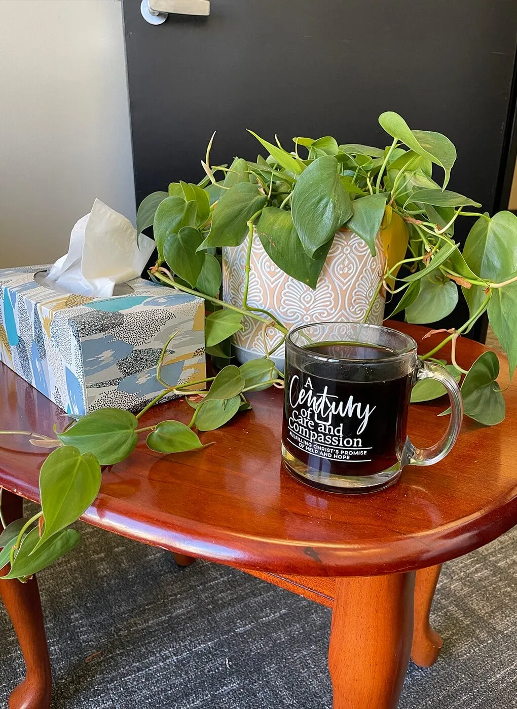 Small table with a plant, tissue box, and a mug that says 