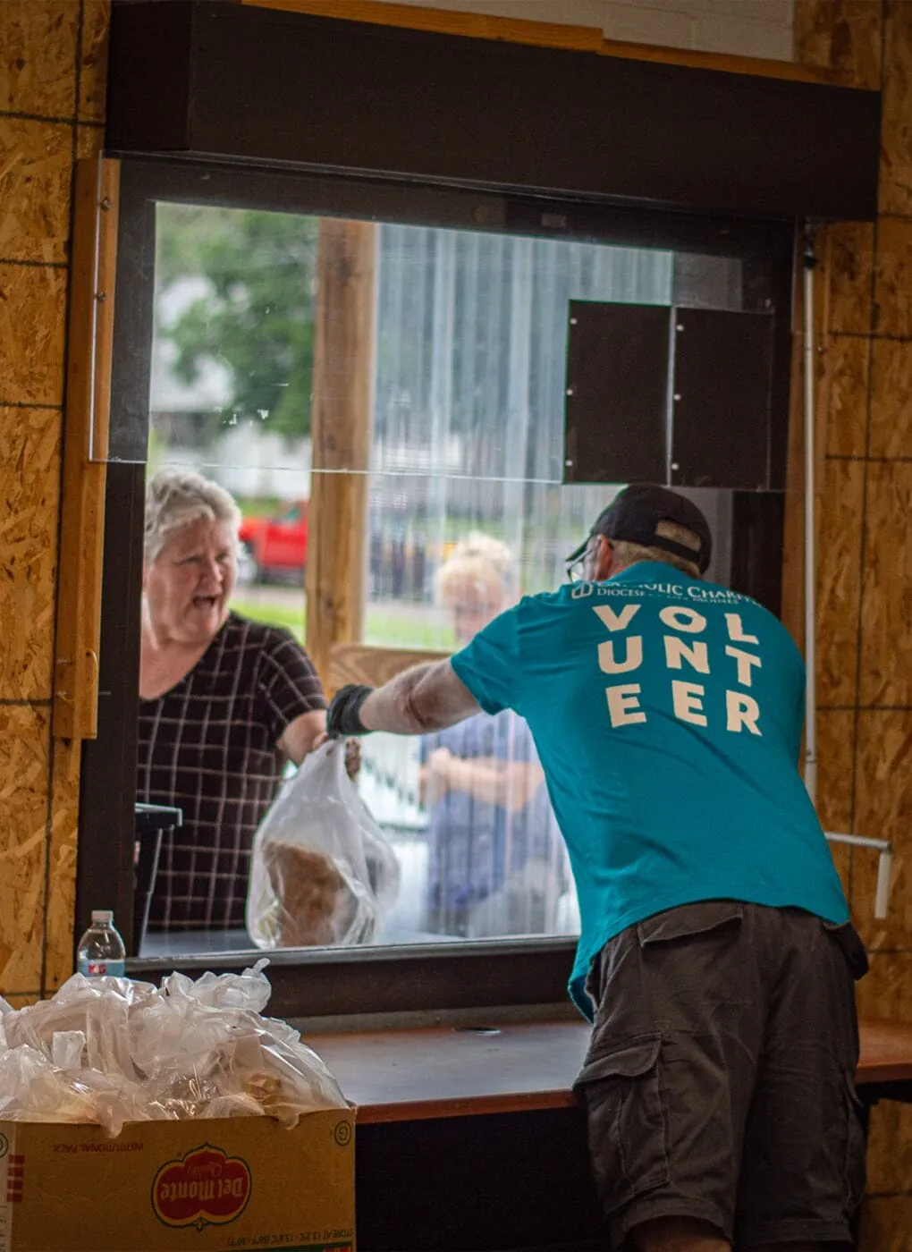 Food pantry volunteer hands a bag of food through the window to a woman