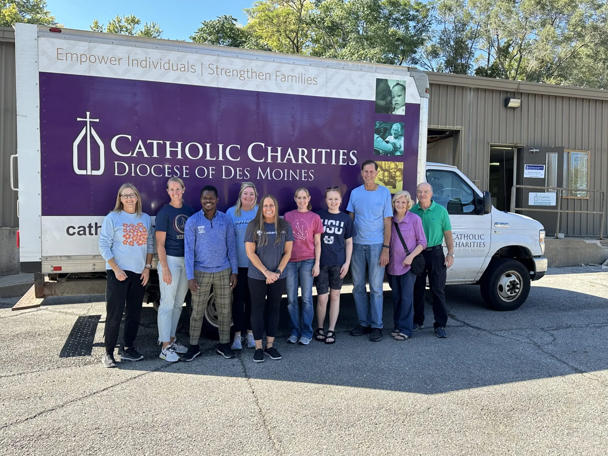 Ten people stand smiling in front of a Catholic Charities box truck.