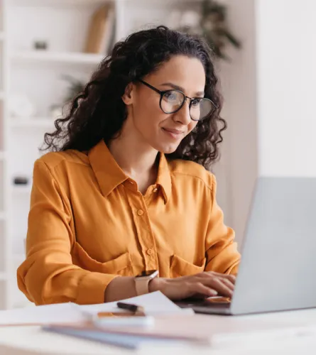 Woman in a yellow shirt smiling while using a laptop