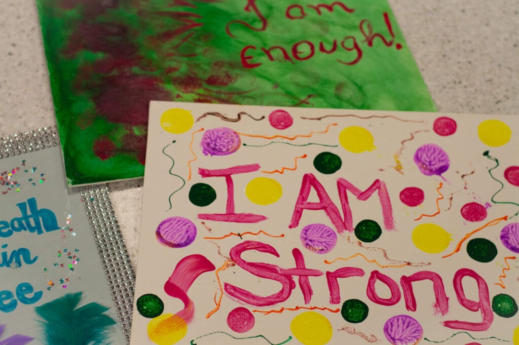 Handmade posters with colorful decorations and empowering phrases, including 'I Am Strong' and 'I am enough.